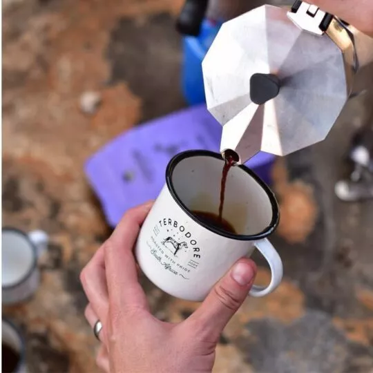 Woman pouring coffee into a Terbodore Tin Cup with rocks in background