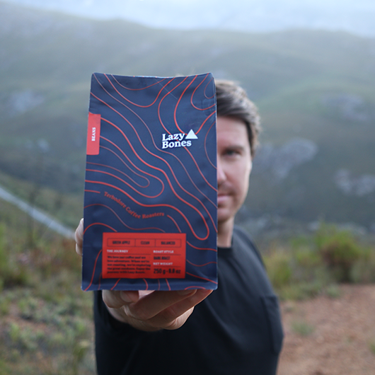 Man holding a Lazy Bones Coffee bag with mountains in the background - Terbodore